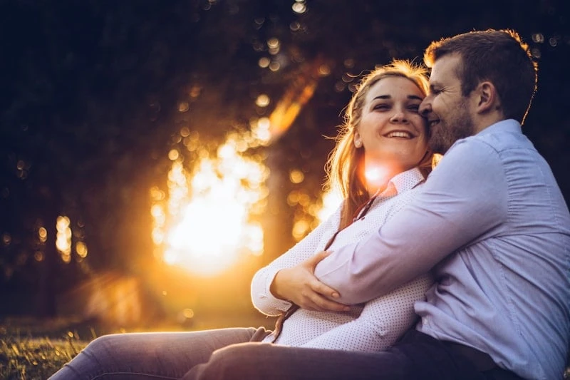 Pareja joven abrazada y sonriendo al atardecer, al aire libre